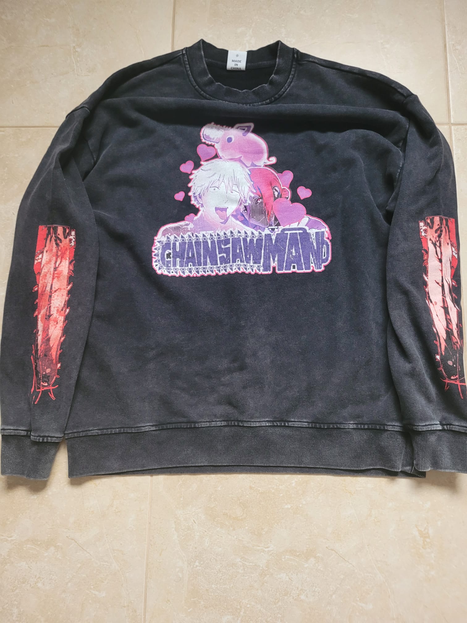 Black sweatshirt with 'Chainsaw Man' graphic design on a beige tiled floor