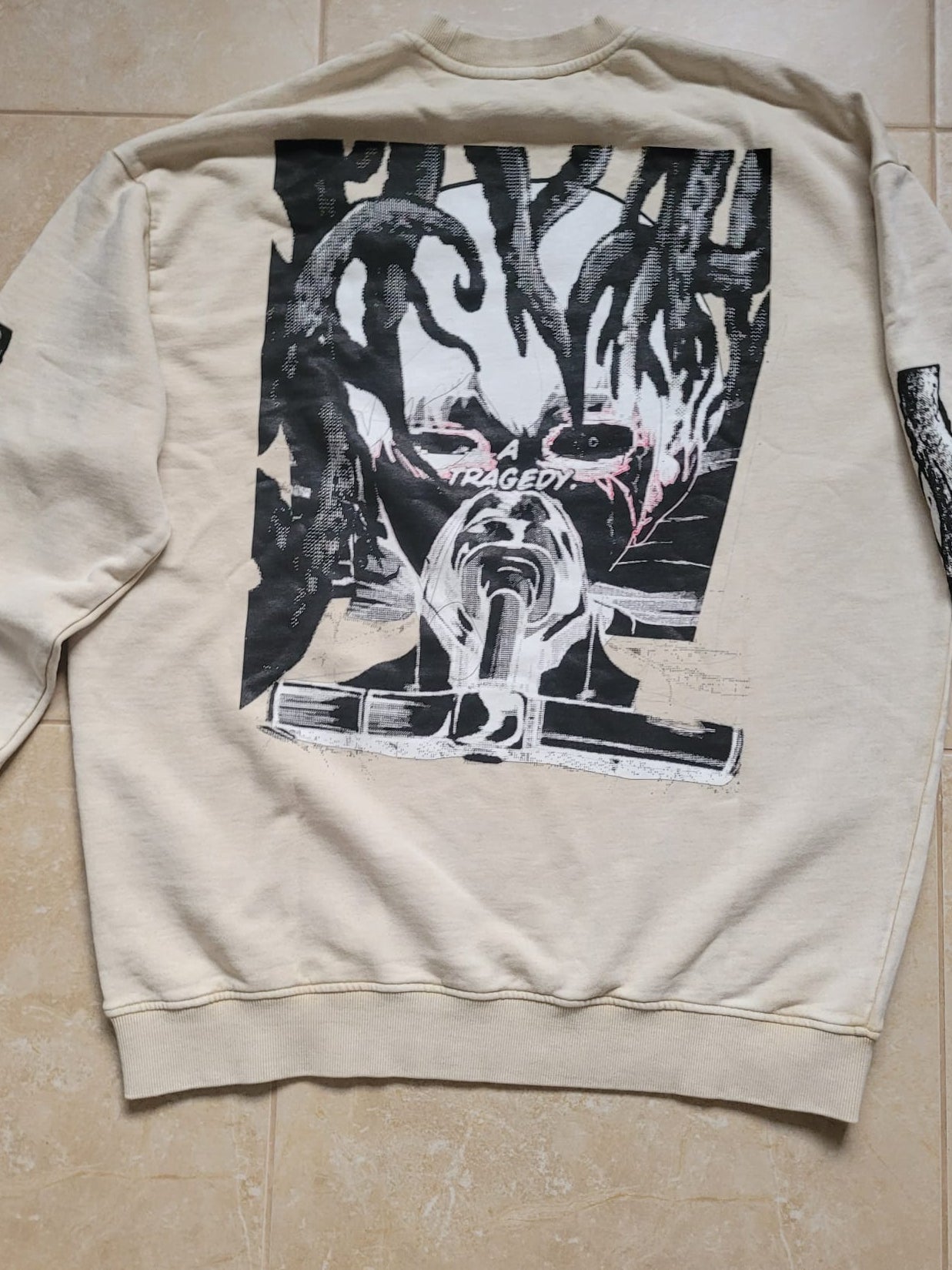 Beige sweatshirt with black graphic design on a tiled floor